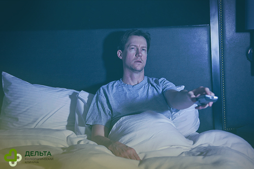 Мужчина смотрит телевизор в кровати ночью