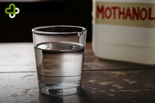 Стакан с жидкостью на фоне канистры Метанола